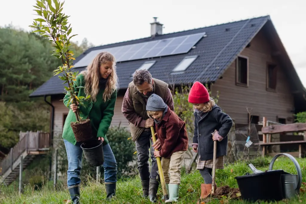 Familie planter et træ i haven foran et hus med solceller – konkret klimahandling og en mere klimavenlig hverdag